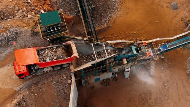Quarry dump truck unloads the rock into a rock crusher. Open pit mine quarrying extractive industry stripping work. Conveyor and production of construction gravel and sand.  