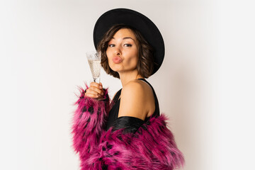 Happy  selebrating woman in stylish fur coat holding glass of shampagne , wearing pink fur coat and black party dress. posing over white background.