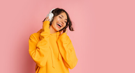 Happy brunette girl  Listenning music and dancing  over pink background. Wearing orange hoodie .