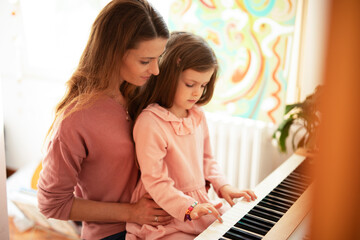 Woman and girl playing a piano. Beautiful mom teaching her daughter playing a piano..