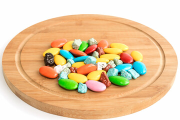 On a wooden surface there are multicolored sweets with chocolate filling and a sweet dessert in bulk. 