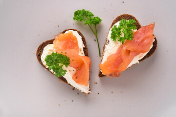 Mini sandwiches with salmon, curd cheese, parsley and rye bread in form of hearts. Valentine's day homemade creative food. Love breakfast design. Selective focus and copy space
