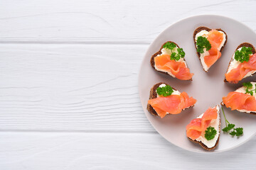 Mini sandwiches with salmon, curd cheese, parsley and rye bread in form of hearts. Valentine's day homemade creative food. Love breakfast design. Selective focus and copy space