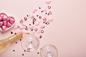 Obraz na płótnie Canvas Valentines day greeting card with champagne bottle, tow glasses, chocolate hearts and gift box on pink background. Top view with space for greetings. Greeting card with copy space.