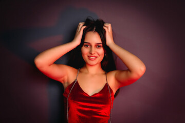 Close up photo of a beautiful happy brunette girl in red clothes touching her hair looking at the camera.