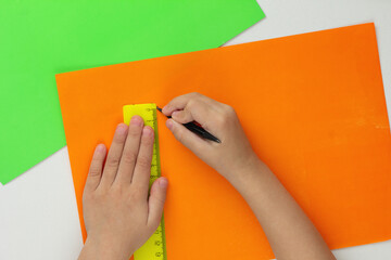 Top view of child hands drawing line using pencil and ruler on orange paper on white background