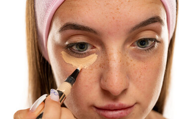 Young freckles  woman applyes concealer under her eyes