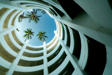 Bottom view multi-story car park building with coconut tree above building in summer. Multi-level...