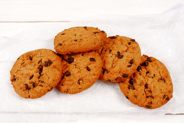 Oatmeal cookies with small pieces of chocolate on parchment paper and a white wooden background.Coffee shop menu concept, cookie recipe