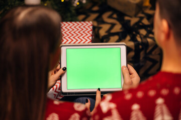 Hands holding a tablet computer with green mock up screen. Caucasian couple using tablet for christmas video call with happy couple on screen. Christmas, festivity and communication technology
