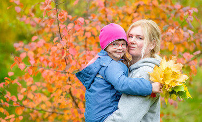 Mother hugs her daughter with Downs syndrom at autumn park. Empty space for text