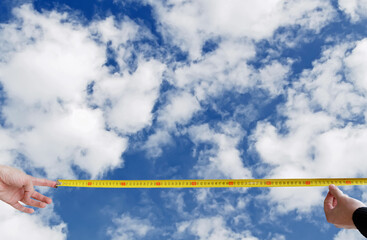 Measuring tool in hand against blue sky background with cumulus clouds