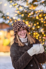 Woman in fur coat, panama hat at Tallinn Christmas market drinking hot mulled wine from reusable cup