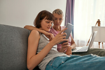 Lesbians watch on digital tablet on sofa at home