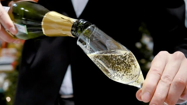 The male hands of the waiter pour a glass of sparkling wine or champagne. Close-up