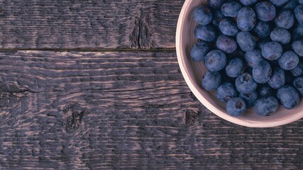 Clay bowl with blueberries on the texture of an old wood. Close-up, flat lay