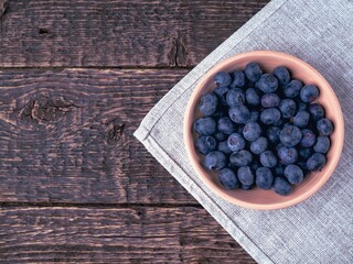 A bowl of blueberries on a gray cloth napkin on a background of an old wooden surface. Close-up, flat lay
