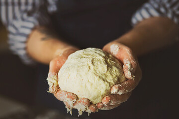 A cook in an apron and a striped shirt holds fresh dough in his hands, from which he will bake bread. Home cooking. The process of preparing the dough.