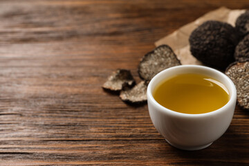 Fresh truffle oil in bowl on wooden table, space for text