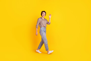 Fototapeta na wymiar Full body profile side photo of young attractive woman walk waving hi arm isolated over yellow color background