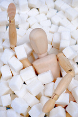 A wooden mannequin doll,strewn with sugar cubes,drowns in a pile of sugar.Unhealthy concept of sugar addiction,obesity and related diseases,diabetes,articles about the dangers of sugar.Vertical photo