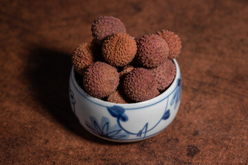 Dried litchi in a bowl on a dark yellow table;