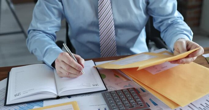 Man sorting letters in yellow envelopes and writing in notebook closeup 4k movie