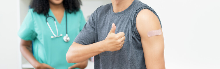 Close up - plaster on arm of man and thumb up after third vaccination against Covid 19