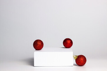 white rectangular box with shadows on a light white background. For cosmetics or cosmetology background. stand for advertising beauty products. Christmas red shiny balls. New Year.