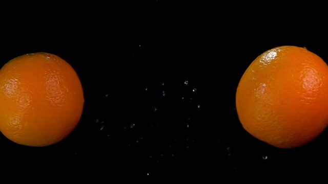 Oranges are colliding with each other rising drops of water on black background