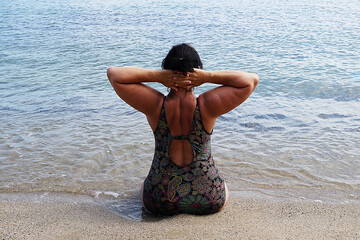 woman in a swimsuit performs yoga while sitting on the shore at the water's edge