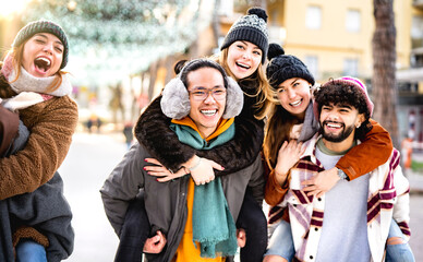 Happy multicultural friends walking at winter travel location on piggyback move - Everyday life style concept with happy guys and girls having fun together outdoors - Warm backlight filter