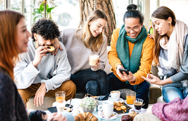 Multicultural friends playing with mobile phone at coffee bar - People having fun together at cafeteria on brunch time - Life style concept with happy men and women at cafe venue - Bright warm filter - 476579759