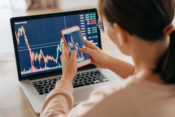 Woman crypto trader investor broker using smartphone app and laptop executing financial stock trade...