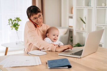 Single mother taking a phone call while holding her baby and using laptop. Happy multitasking...