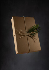 Simple Christmas Time Giftbox on a Black Grunge Background. Packaging with a Christmas Gift, Made of Natural Cardboard, Rough Rope and a Branch of Green Pine in the Soft Light of the Day.