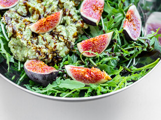 Fig salad with soft cheese and blueberries, avocado, arugula, balsamic sauce in steel bowl. Food closeup. Healthy vegetarian salad.