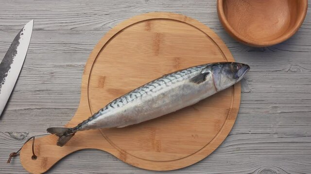 Top view of the male hands putting the round wooden board with the mackerel fish