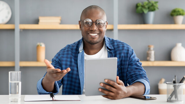 Happy mature african american man holding digital tablet and talking to camera, recording video, sitting at home office - Powered by Adobe