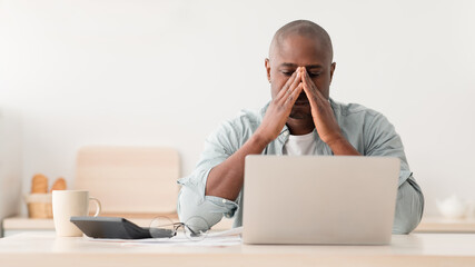 Depressed mature african american man calculating taxes and being disappointed because of expensive modern life