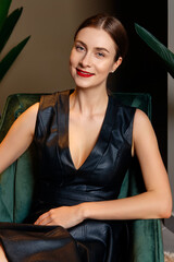 Portrait of happy lady in faux leather dress sitting in armchair at home