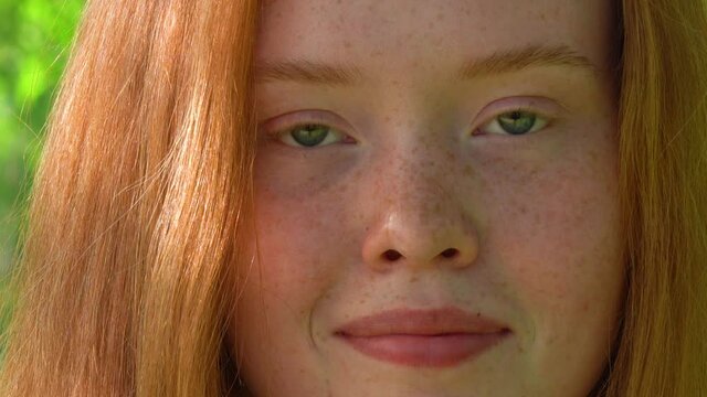 The face of a beautiful red-haired girl in backlight. Portrait a smiling young woman with red hair and freckles against the backdrop of a bright sunny meadow. Natural beauty with freckles