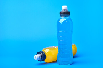 Standing and lying isotonic energy orange yellow and blue sport drink in plastic bottles on blue...