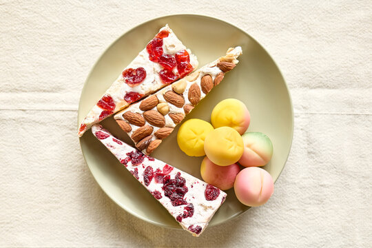 Marzipan fruits and soft nougat with fruits and almond in the plate on white linen tablecloth. Martorana fruit molded a shape of peaches. Typical sicilian pastries - frutta Martorana.