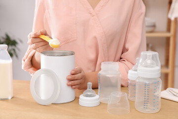 Woman preparing infant formula at table indoors, closeup. Baby milk