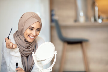 Muslim woman is applying compact powder looking at mirror