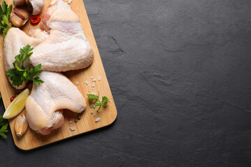 Wooden board with fresh raw chicken wings and other products on black table, top view. Space for text