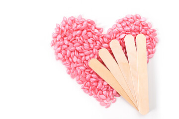 pink wax for depilation in granules, in the shape of a heart and wooden sticks - obrazy, fototapety, plakaty
