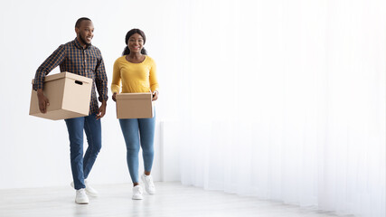 Fototapeta na wymiar Relocation Concept. Young African American Spouses Walking With Cardboard Boxes Near Window