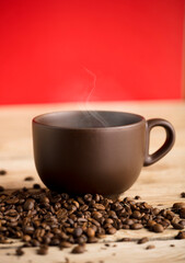 brown coffee cup with hot steam smoke and beans on wooden table, red background